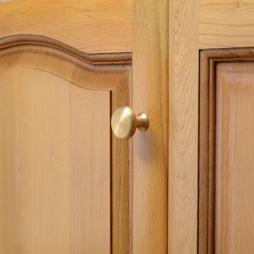 solid brass cupboard knob with classic shape, mounted to wooden cupboard door.