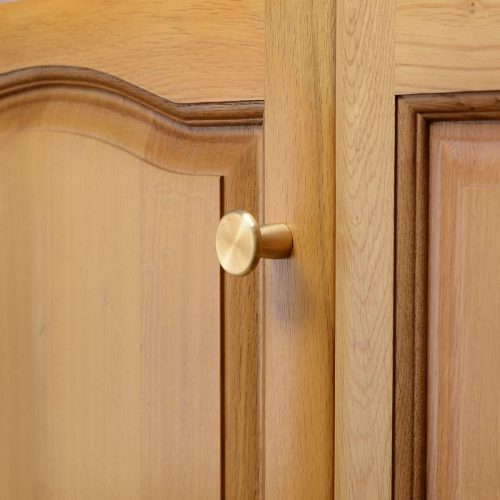 solid brass cupboard knob with a mushroom shape, mounted to a wooden cupboard door.