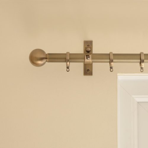 solid brass ball shaped curtain finial, mounted to curtain rail, in antique finish